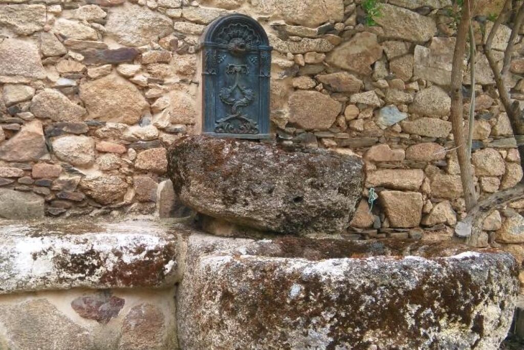 Un muro de piedra con una puerta de metal y una roca grande al frente.