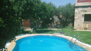 A swimming pool with a metal ladder, surrounded by greenery and a stone building. - Tictágora House: House 1 (Plasenzuela)