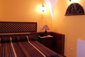 A room with a bed, a nightstand, a lamp, and a wall-mounted shelf.