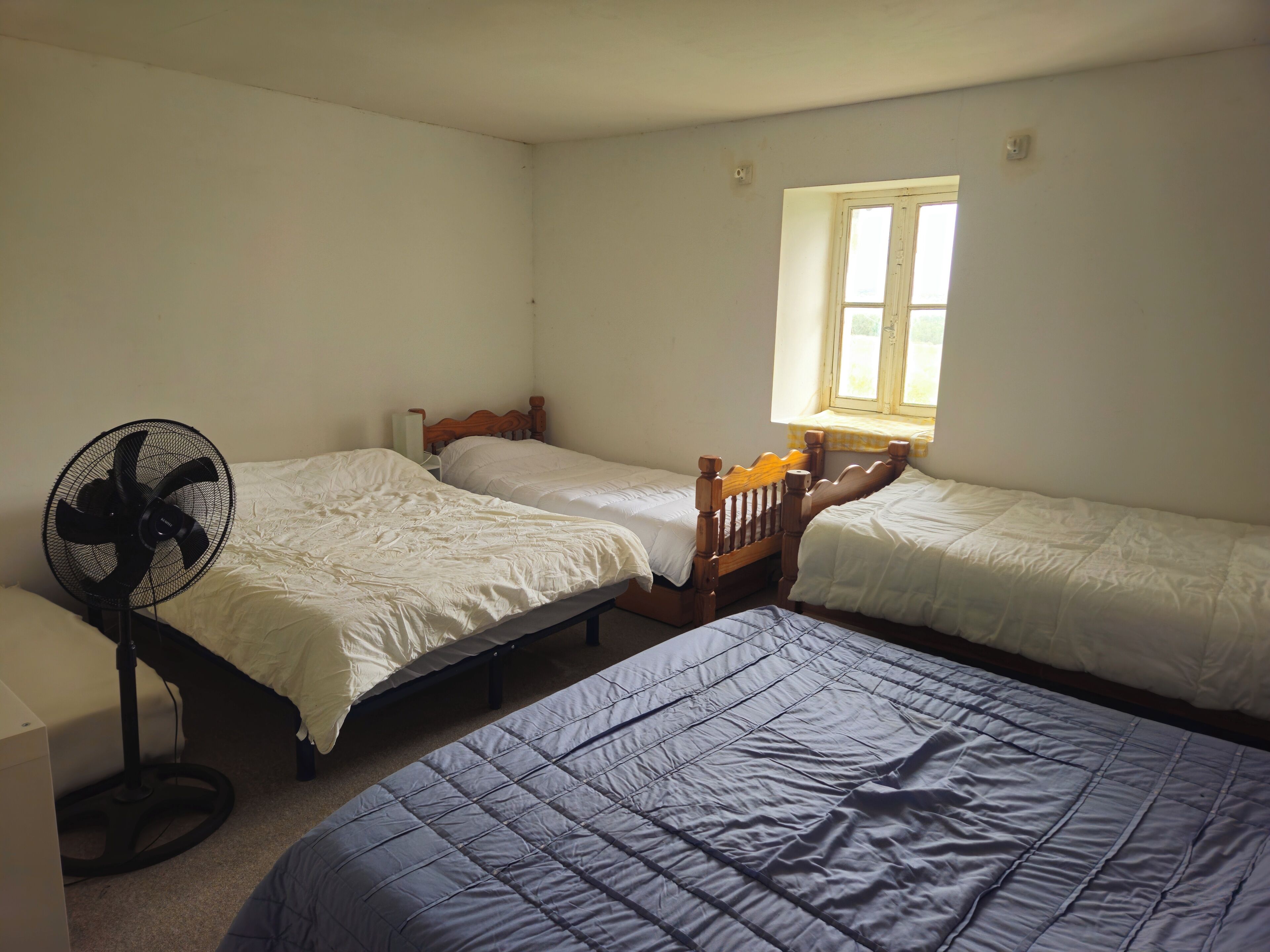 Een kamer met drie eenpersoonsbedden, een ventilator en een raam met uitzicht.