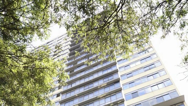 Ein Hochhaus mit mehreren Etagen, großen Fenstern und einem Baum im Vordergrund.