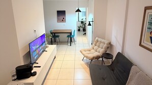 Ein modernes Wohnzimmer mit Flachbildfernseher, einer Couch, einem Essbereich mit Stühlen und einer Küchenzeile im Hintergrund.
