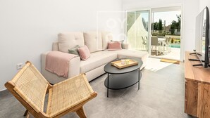 Een moderne woonkamer met een bank, een rieten stoel, een salontafel en een televisie op een houten dressoir.