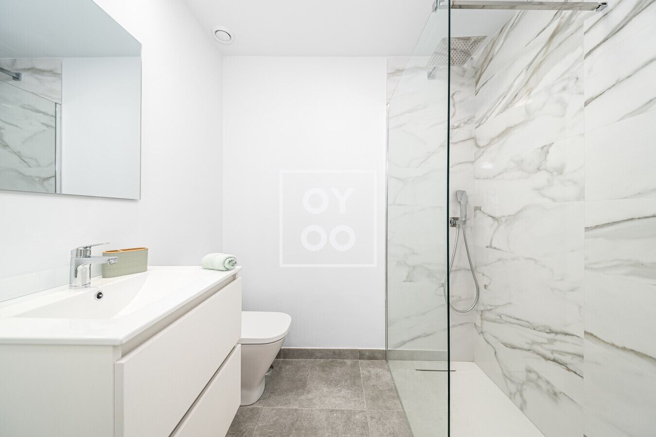 A modern bathroom with a white sink, toilet, and glass shower enclosure.
