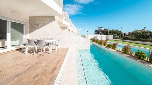 Een modern buitenzwembad met houten terras, een zithoek met stoelen en een helder uitzicht op het omliggende landschap.
