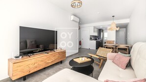 Een moderne woonkamer met een bank, een houten console en een televisie, en een eethoek met tafel en stoelen.