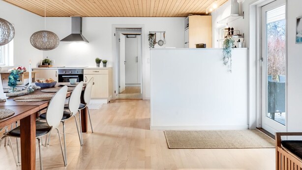 Une cuisine moderne avec un plancher en bois, un coin repas avec une table et des chaises en bois, et une vue sur l’extérieur grâce à une porte-fenêtre coulissante.