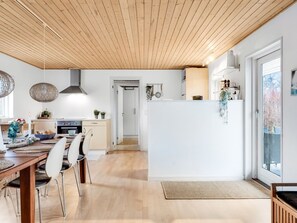 Una cocina moderna con suelo de madera, un comedor con mesa y sillas de madera, y vistas al exterior a través de un ventanal corredero.