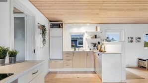 Une cuisine moderne avec des meubles en bois, un réfrigérateur encastré et une fenêtre donnant sur un immeuble bleu.
