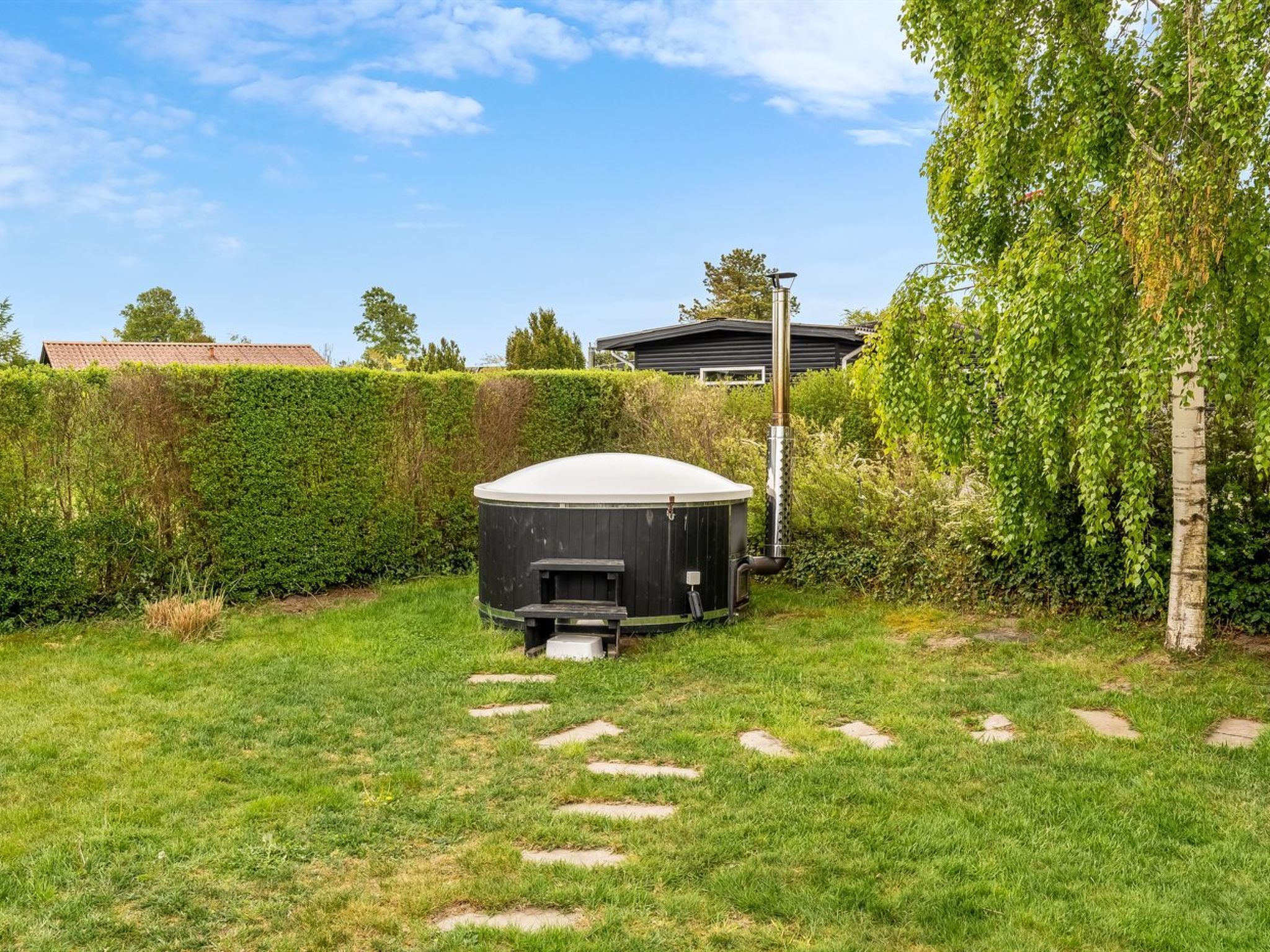 Ein Garten mit Whirlpool, einer Holzterrasse und einer Hecke.