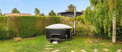 Ein Garten mit Whirlpool, einer Holzterrasse und einer Hecke.