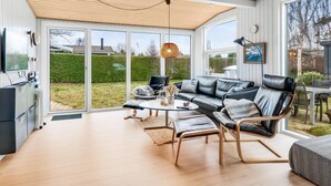 Un salon moderne doté d’une grande porte vitrée donnant sur un jardin, d’un canapé en cuir noir, d’un plancher en bois et d’un ventilateur de plafond.