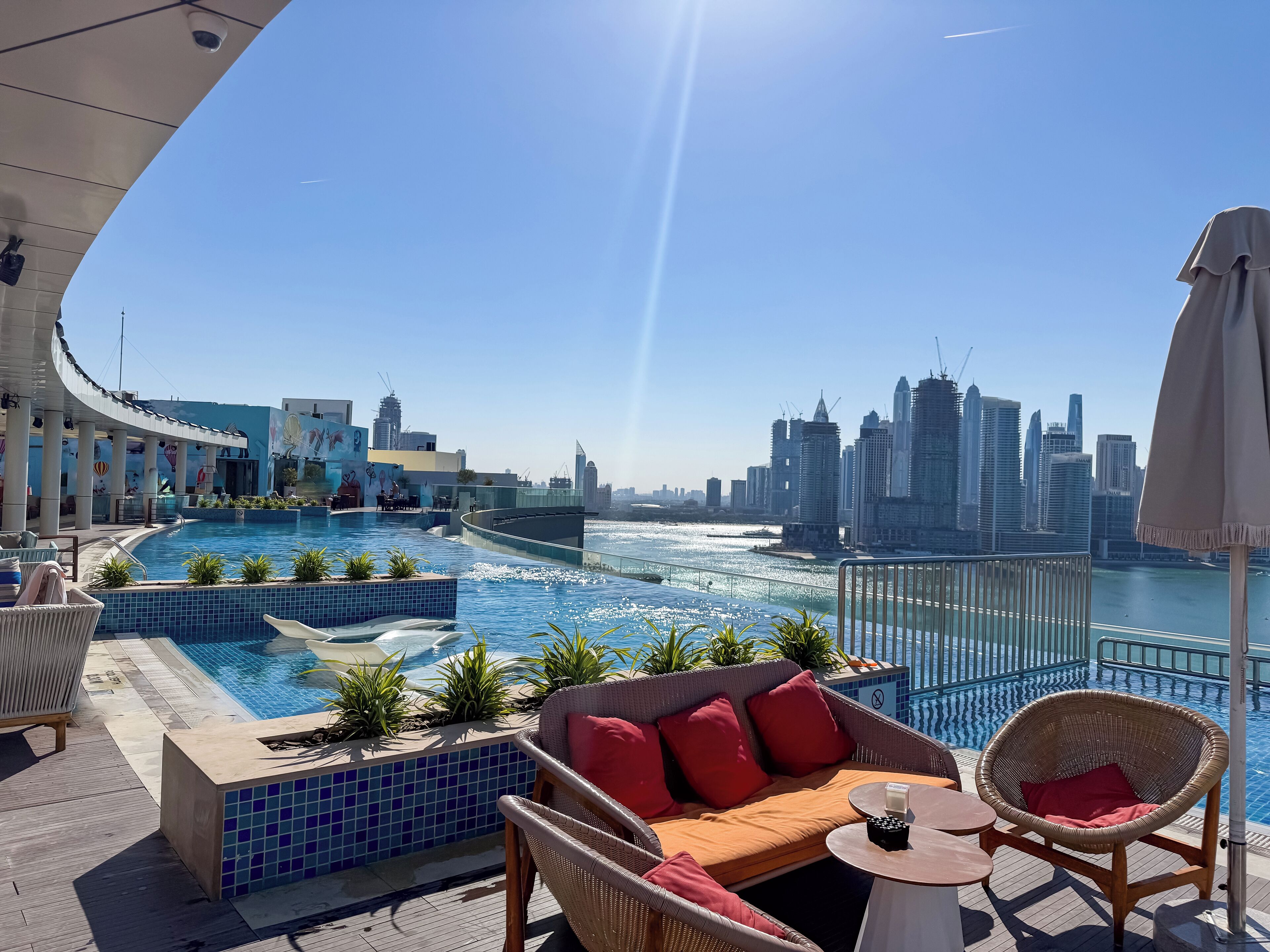 A rooftop pool with a city skyline view, lounge chairs, and a small table.