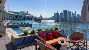 A rooftop pool with a city skyline view, lounge chairs, and a small table. - PVH - Seven Palm - Studio Beach Access (Dubai)