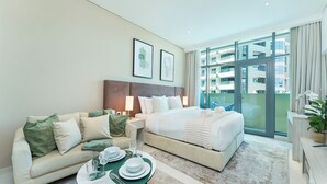 A hotel room with a bed, a sofa, a dining table with plates and glasses, and a large window with a view of buildings. - PVH - Seven Palm - Studio Beach Access (Dubai)