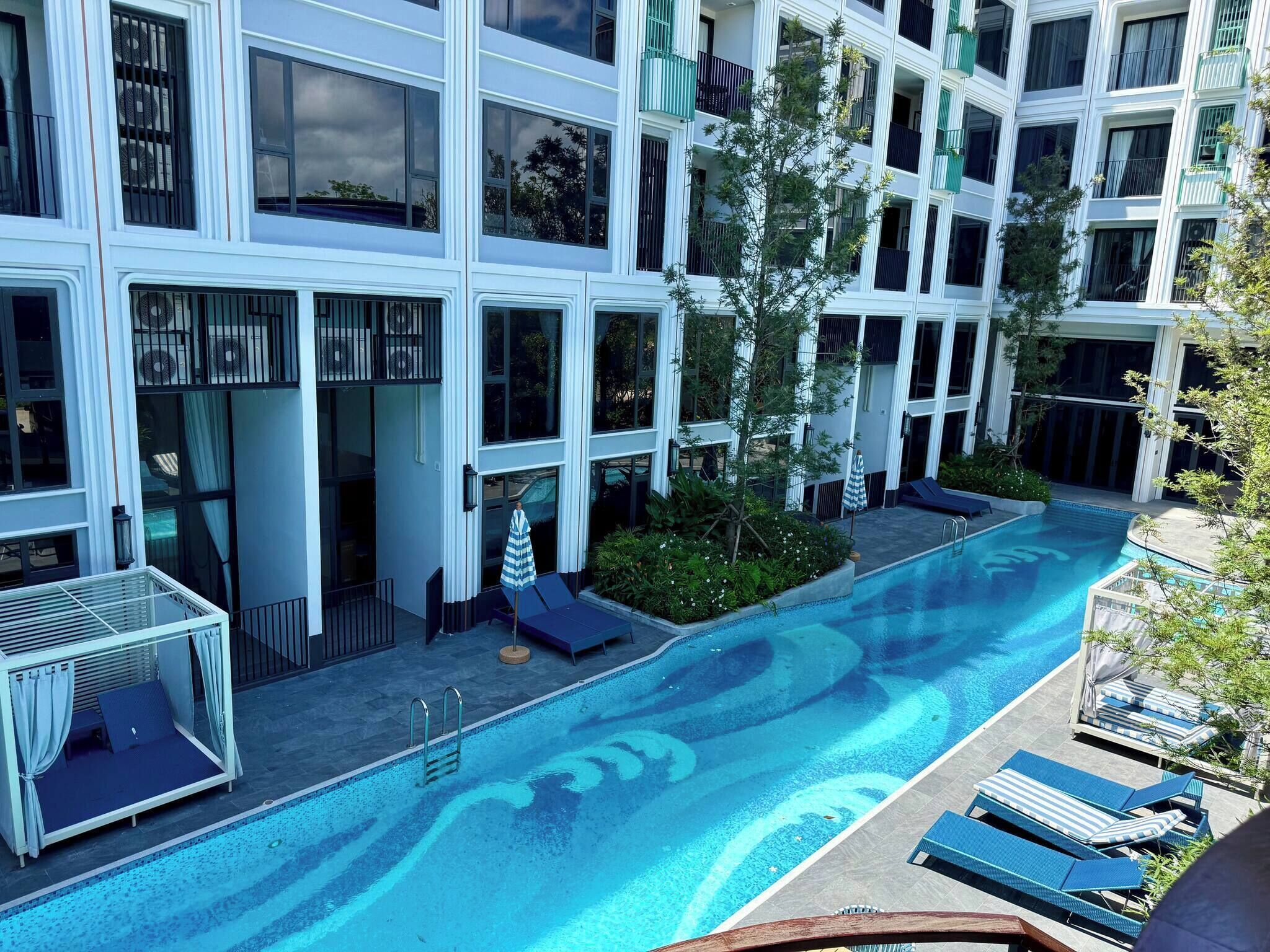 A modern hotel with a large outdoor swimming pool, multiple balconies, and lounge areas.