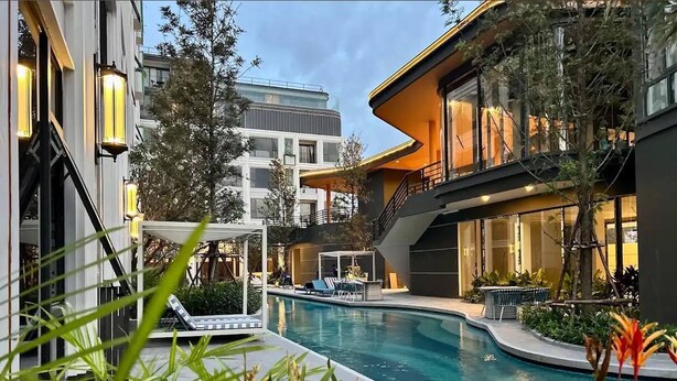 Et moderne hotel med swimmingpool, udendørs siddepladser og frodig beplantning.