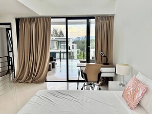 Ein modernes Hotelzimmer mit einem großen Bett, einem Schreibtisch mit Stuhl, einem Laptop und Blick auf einen Berg sowie ein Gebäude durch die Glasdoor.