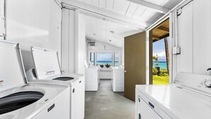 Une buanderie avec des appareils électroménagers blancs, une vue sur l’océan et une porte donnant sur un balcon avec vue sur la plage.