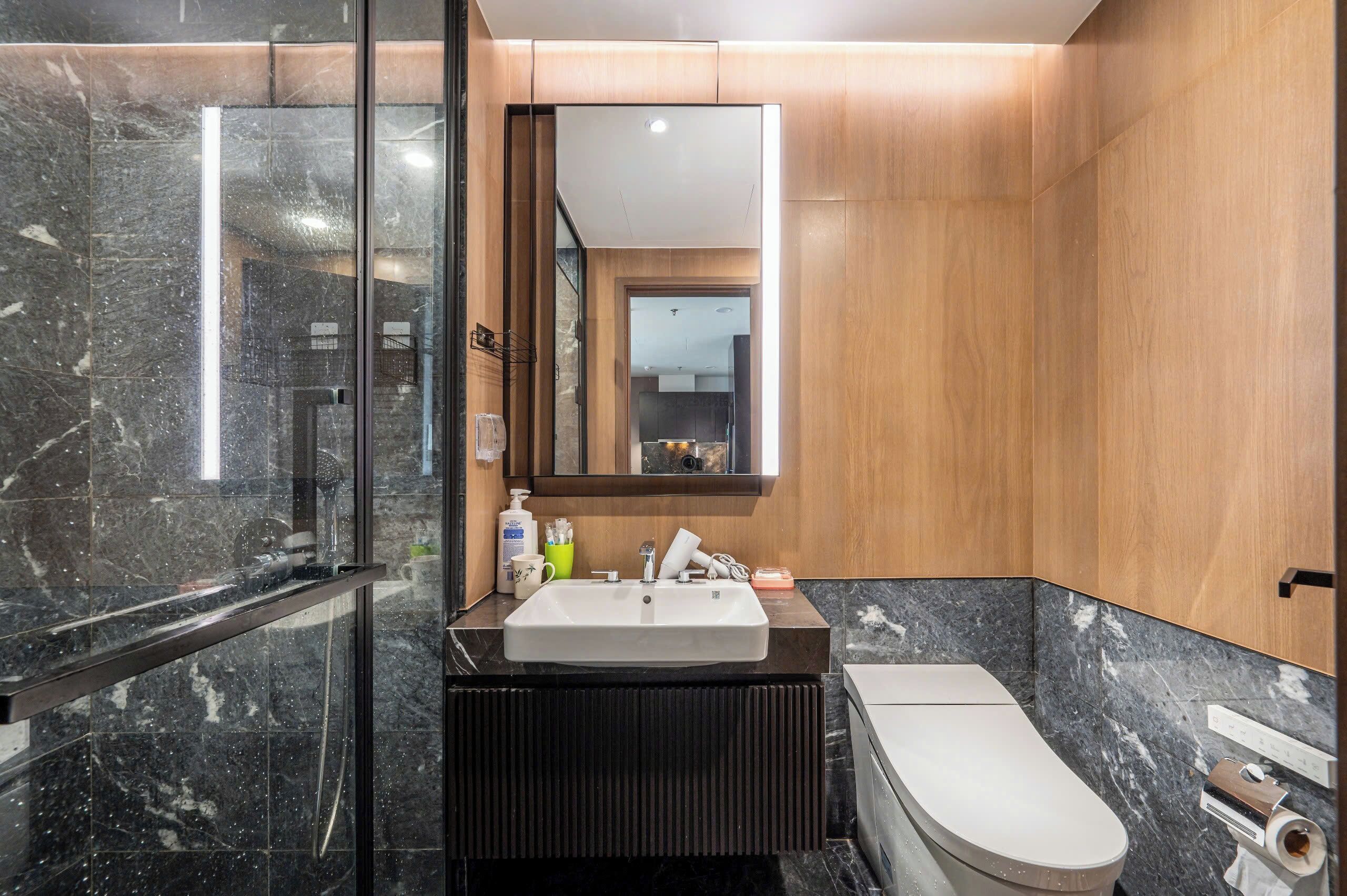 A modern bathroom with a marble sink, a toilet, and a glass shower enclosure.