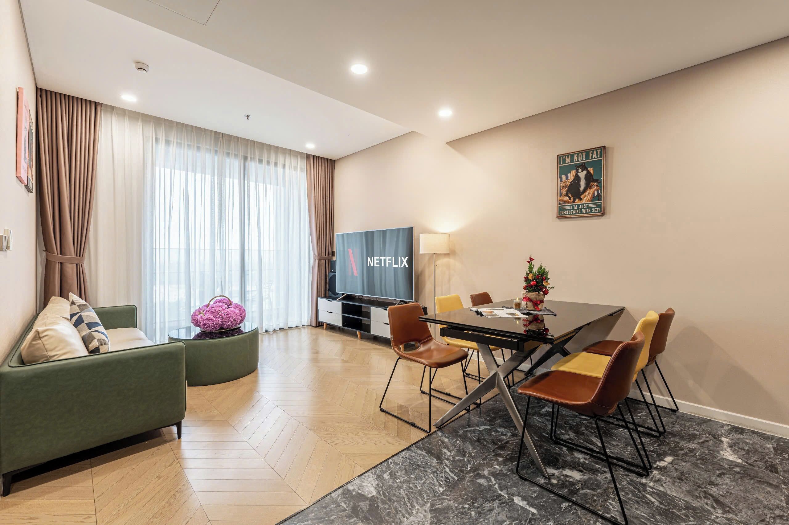 A modern living room with a green sofa, a dining table with chairs, a TV, and a lamp.