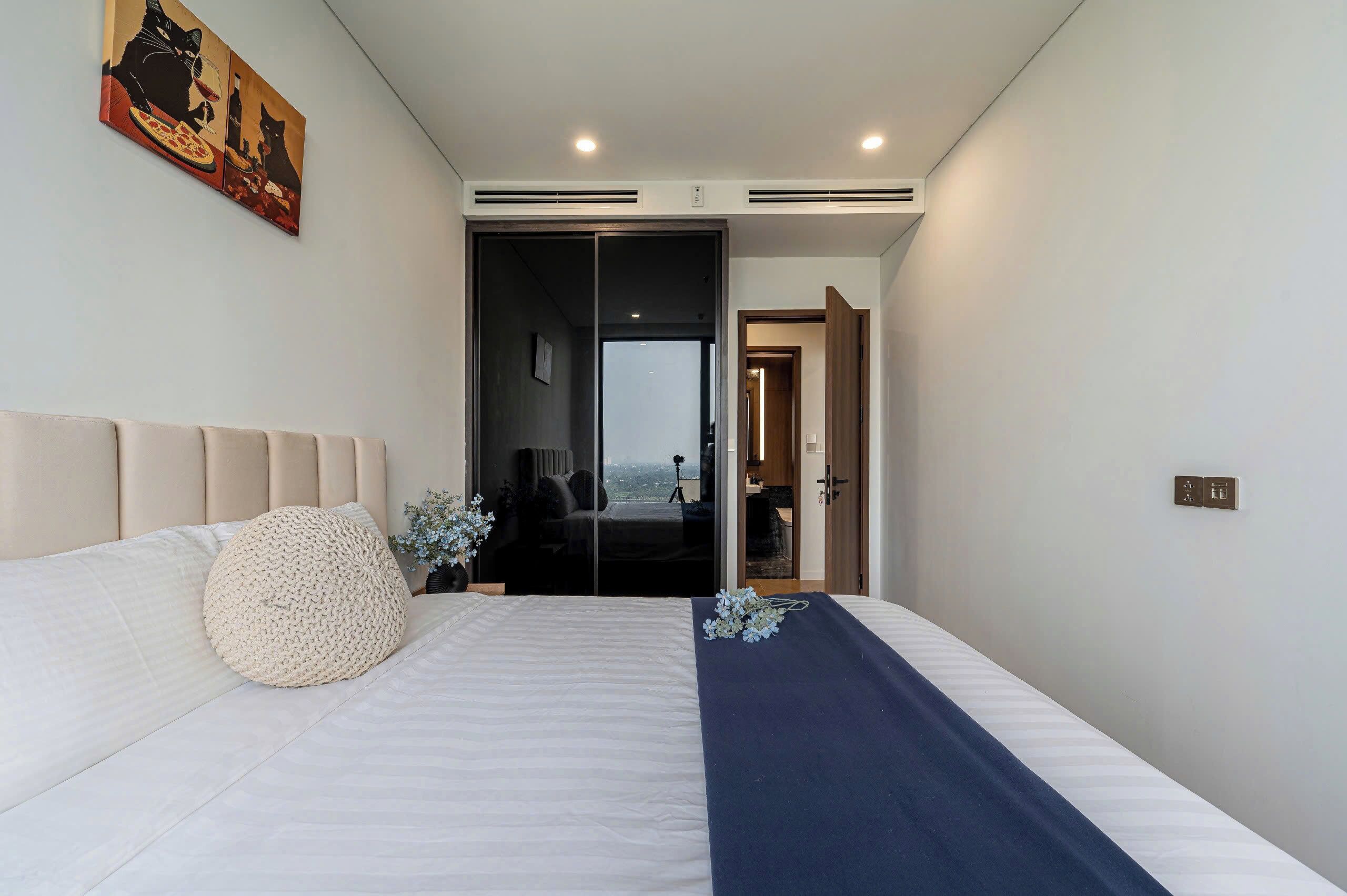 A modern bedroom with a large bed, a view through a sliding door, and a painting on the wall.