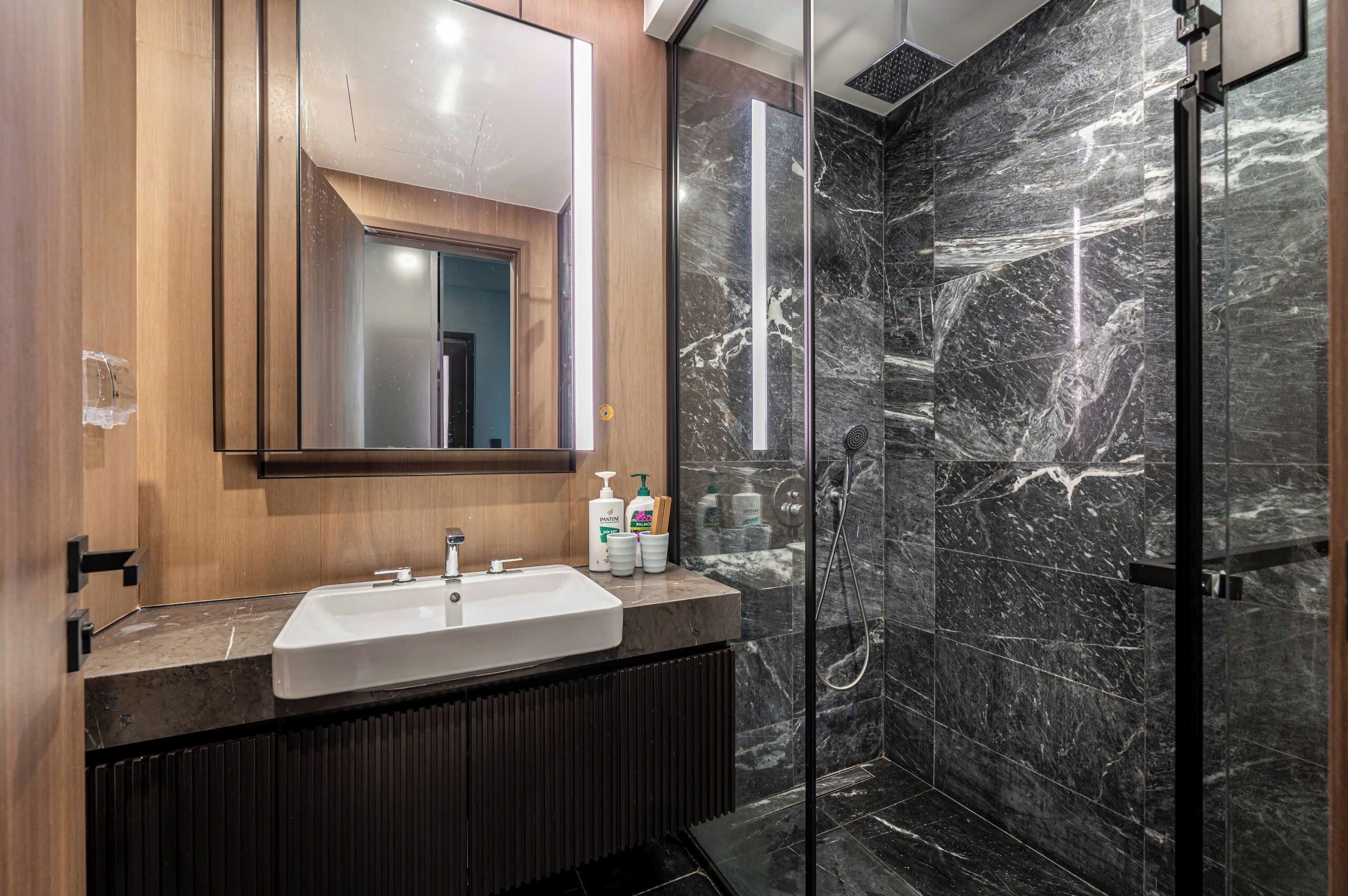 A modern bathroom with a large mirror, a white sink, and a glass-enclosed shower.