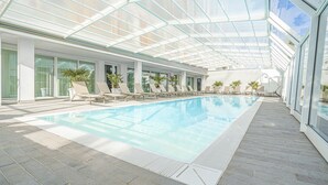 A modern indoor swimming pool with glass ceiling, lounge chairs, and potted plants. - Modern, tastefully furnished hotel room of approximately 28 square meters, featuring a double bed and a single bed, a bathroom with a bathtub or shower, and a large balcony furnished with a table and chairs.Use of the pool and gymUnlimited access to the  (Olbia)