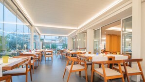 A spacious indoor area with tables and chairs, large windows, and a view of the outside. - Modern, tastefully furnished hotel room of approximately 28 square meters, featuring a double bed and a single bed, a bathroom with a bathtub or shower, and a large balcony furnished with a table and chairs.Use of the pool and gymUnlimited access to the  (Olbia)