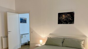 Een slaapkamer met een bed, nachtkastje, plafondventilator, radiator en een deur naar een andere kamer.