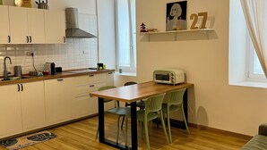 Een kleine keuken met witte kastjes, een houten aanrecht, een plafondventilator en een raam met gordijnen.