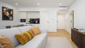 A modern living room with a white sofa, a patterned rug, and a kitchen in the background. - Aspasios Picaria Apartments (Porto)