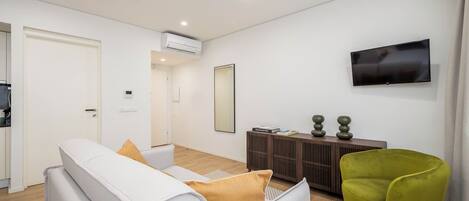 Una sala de estar moderna con un sofá, un sillón verde, un televisor y una mesa consola con adornos.