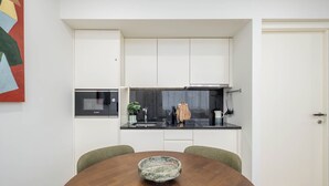 A modern kitchen with white cabinets, a black countertop, and a round wooden table with a bowl. - Aspasios Picaria Apartments (Porto)