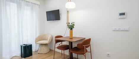 Un salon moderne avec une table à manger en bois, quatre chaises, une petite table d’appoint, un lampadaire, un téléviseur et un thermostat.