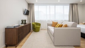 A modern living room with a sofa, a green armchair, a wooden console, and a TV mounted on the wall. - Aspasios Picaria Apartments (Porto)