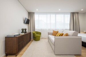 Una sala de estar moderna con un sofá, un sillón verde, una consola de madera y un televisor montado en la pared.