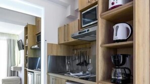 A compact kitchen with wooden cabinetry, a microwave, a coffee maker, and a dishwasher. - Marthina Luxury Living (Nea Propontida)