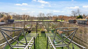 Eine Terrasse mit zwei Metallstühlen und einem Glastisch, umgeben von einem Bambuszaun und Kübelpflanzen.