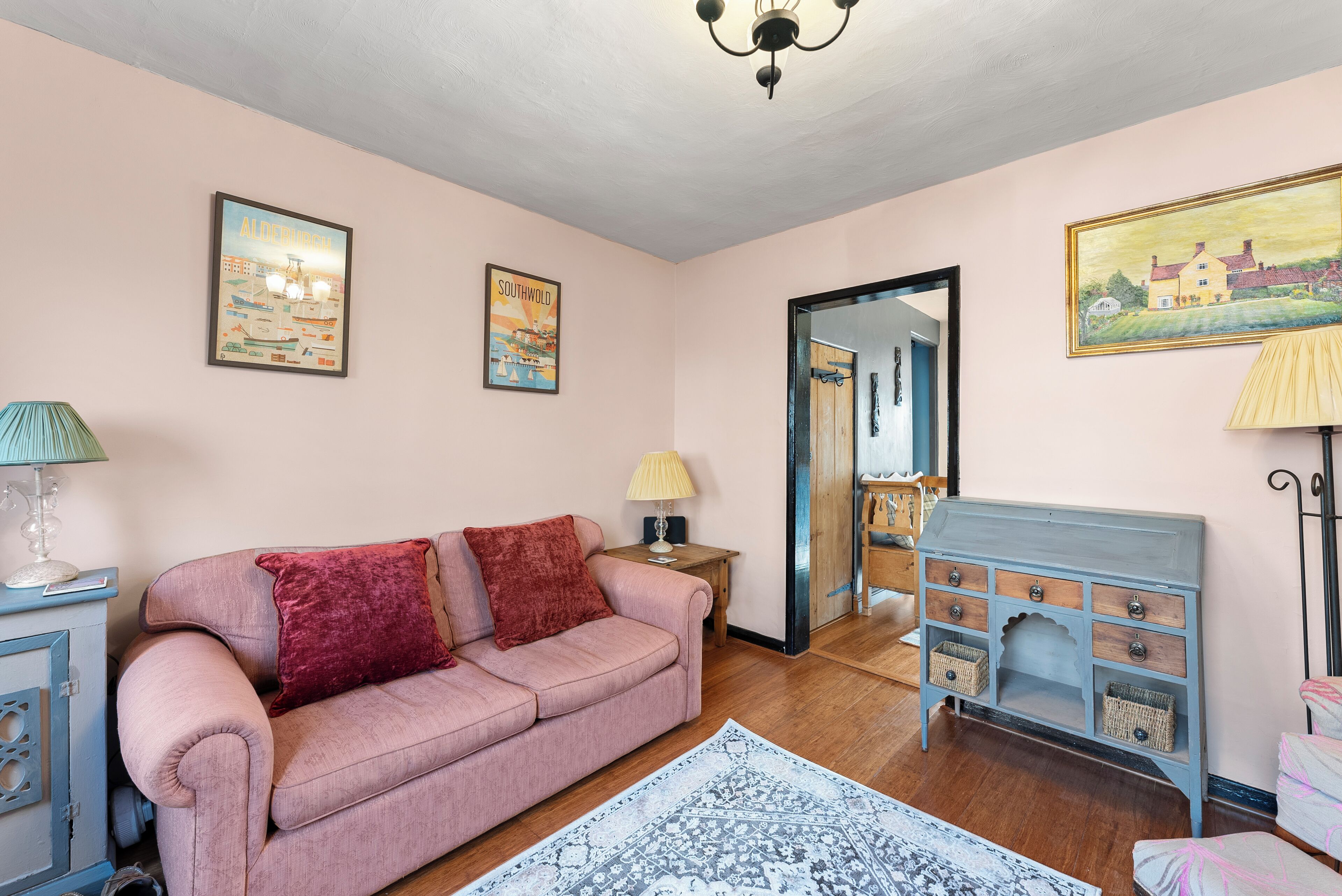 Uma sala de estar acolhedora com um sofá rosa, um tapete estampado, um armário de madeira e uma cômoda azul com gavetas.