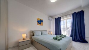 Quarto moderno com cama, mesas de cabeceira, um quadro e vista da cidade por grandes janelas.