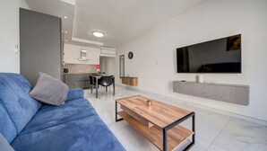 Uma sala de estar moderna com um sofá azul, uma mesa de centro de madeira e uma TV fixada na parede.