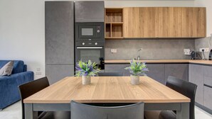 Uma cozinha moderna com uma mesa e cadeiras de madeira, duas plantas em vasos e eletrodomésticos embutidos.