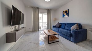 Uma sala de estar moderna com televisão de tela plana, um sofá azul, uma mesa de centro de madeira e um quadro na parede.