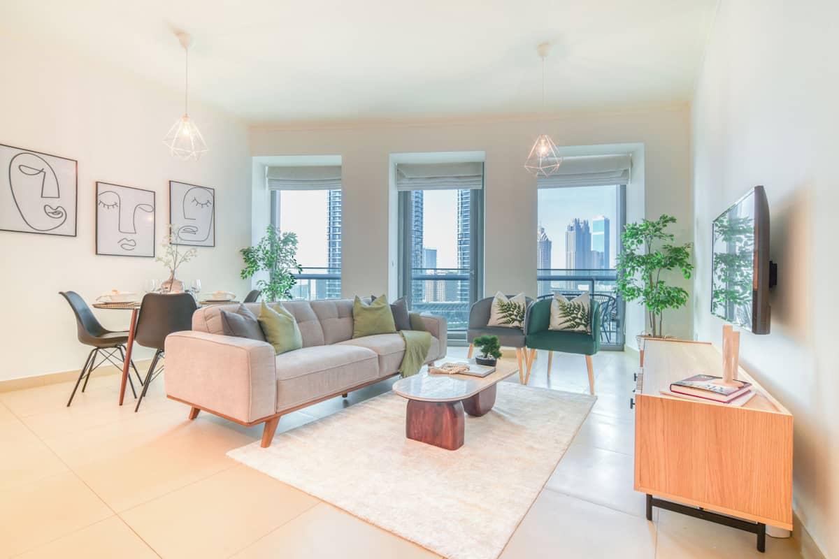 Ein modernes Wohnzimmer mit einer Couch, einem Couchtisch und Sesseln. Große Fenster bieten Blick auf die Stadt.