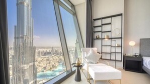 A modern bedroom with a large window offering a city view, a white sofa, a bedside table, and a bookshelf. - Burj Vista 1- Mint Stay (Dubai)