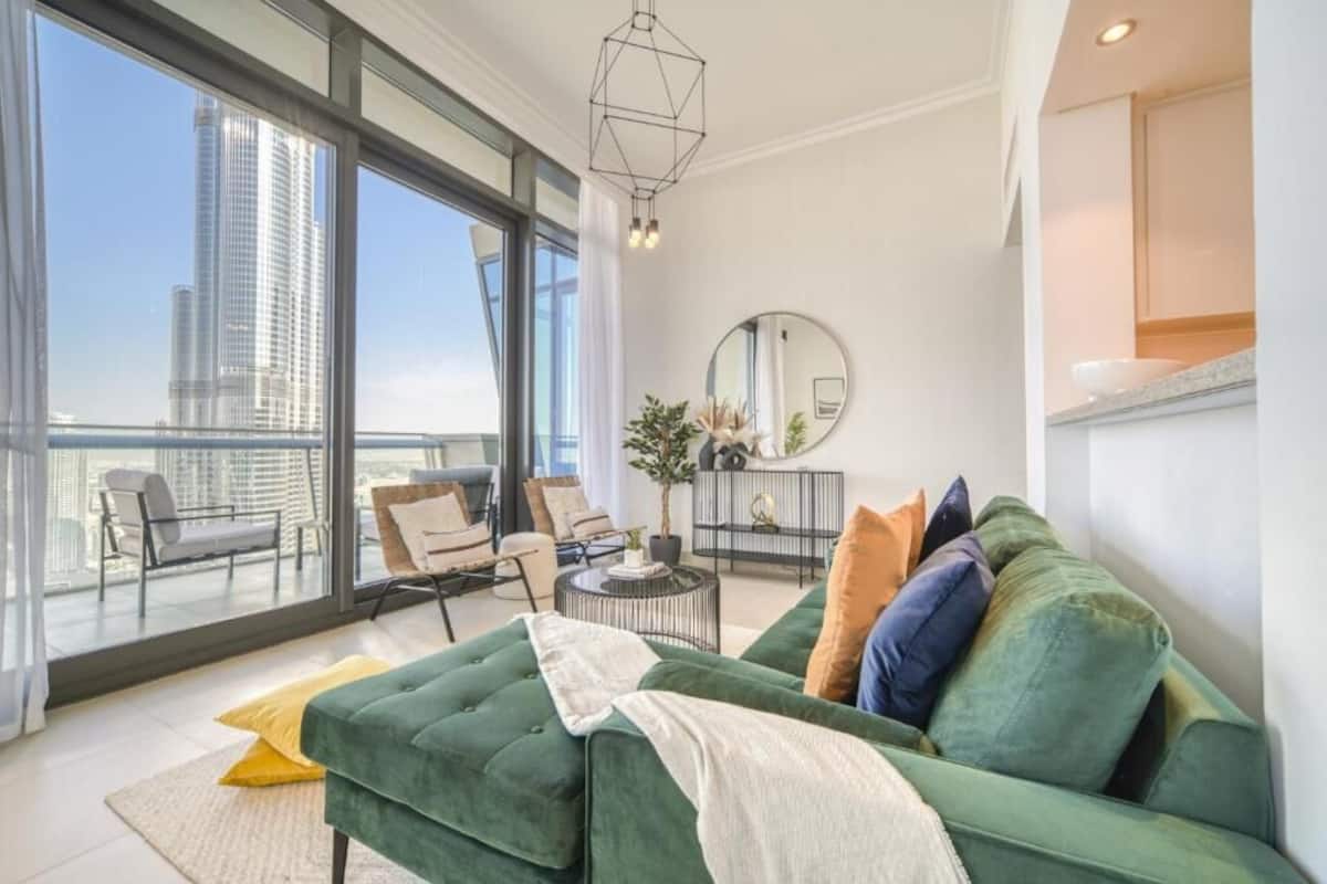 Ein modernes Wohnzimmer mit einem grünen Sofa, einem runden Couchtisch und Blick auf eine Stadtlandschaft durch große Fenster.