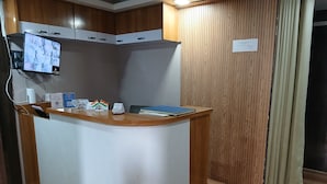 Un comptoir d’accueil avec un écran d’ordinateur, un téléphone et un classeur bleu. Au-dessus du comptoir, on trouve des armoires en bois, et un mur recouvert de panneaux de bois se trouve sur le côté droit.