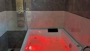 Une salle de bain moderne avec une douche à parois de verre, une baignoire à remous dotée d’un éclairage rouge et des murs en marbre.