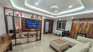 Un salon moderne avec un téléviseur à écran plat, des étagères en bois ornées d’objets décoratifs, un canapé et une table basse.